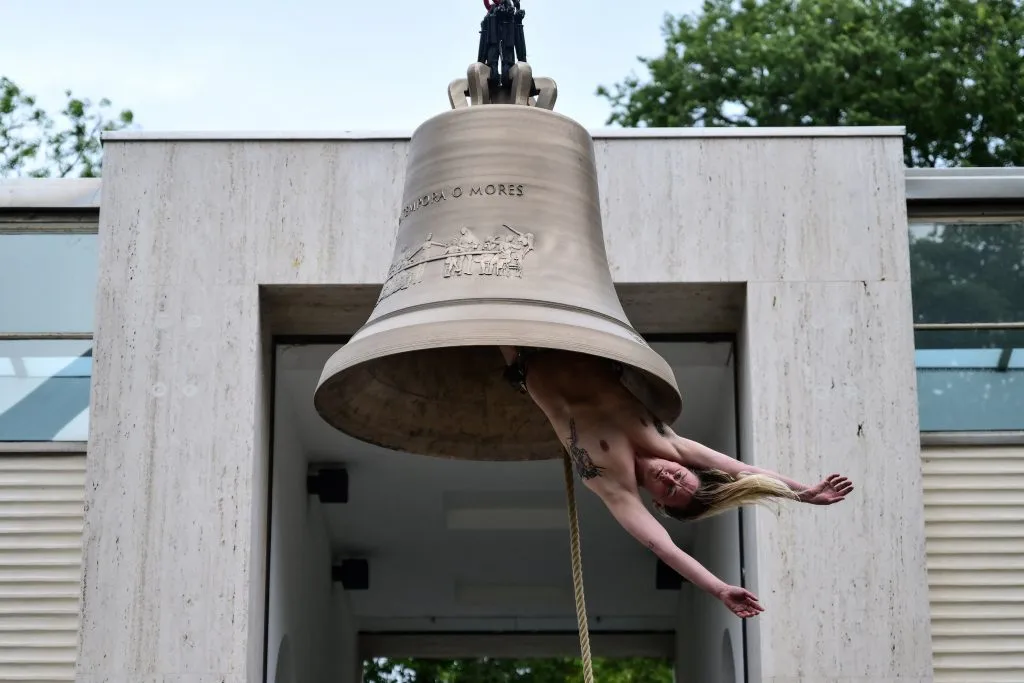 Performance artística con una campana y un artista colgando