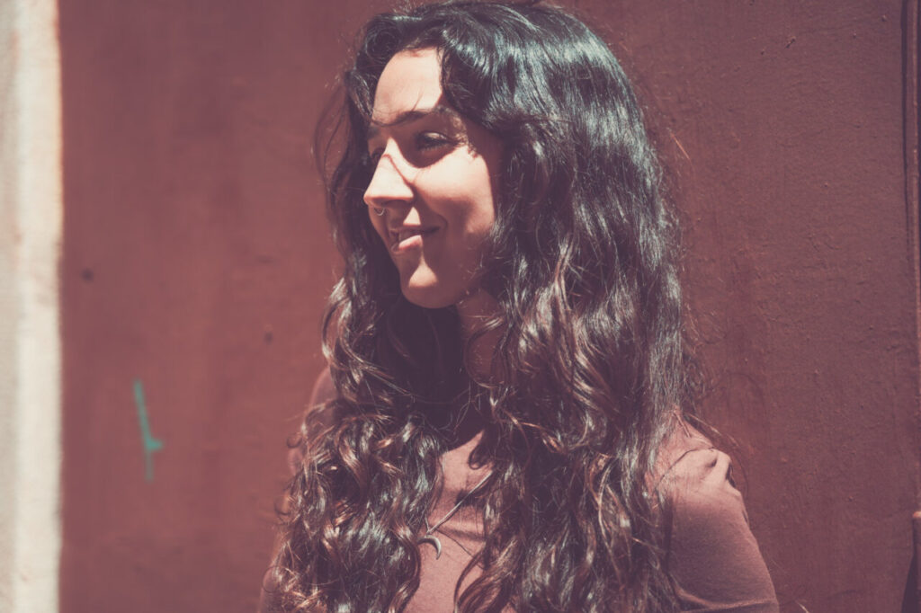 Mujer con cabello rizado sonriendo frente a una pared colorida