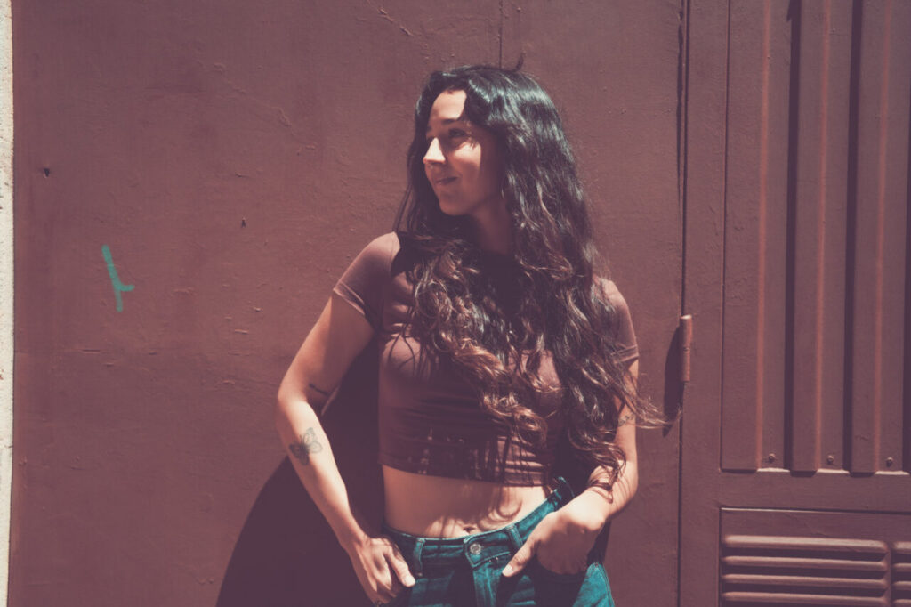 Mujer con cabello largo y rizado posando frente a una pared marrón