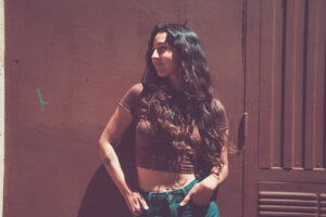 Mujer con cabello largo y rizado posando frente a una pared marrón