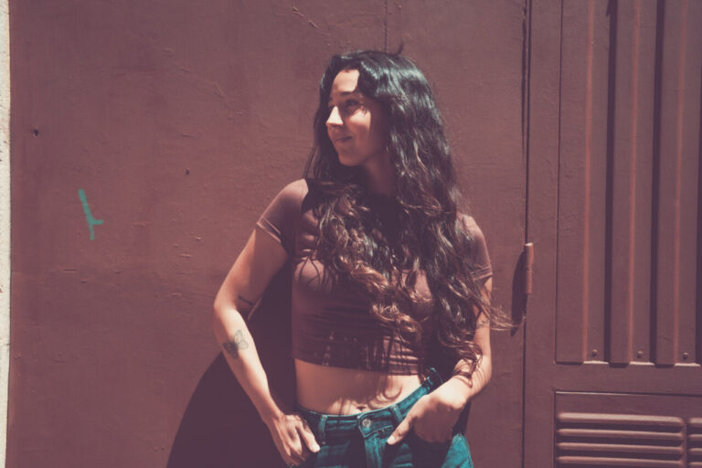Mujer con cabello largo y rizado posando frente a una pared marrón