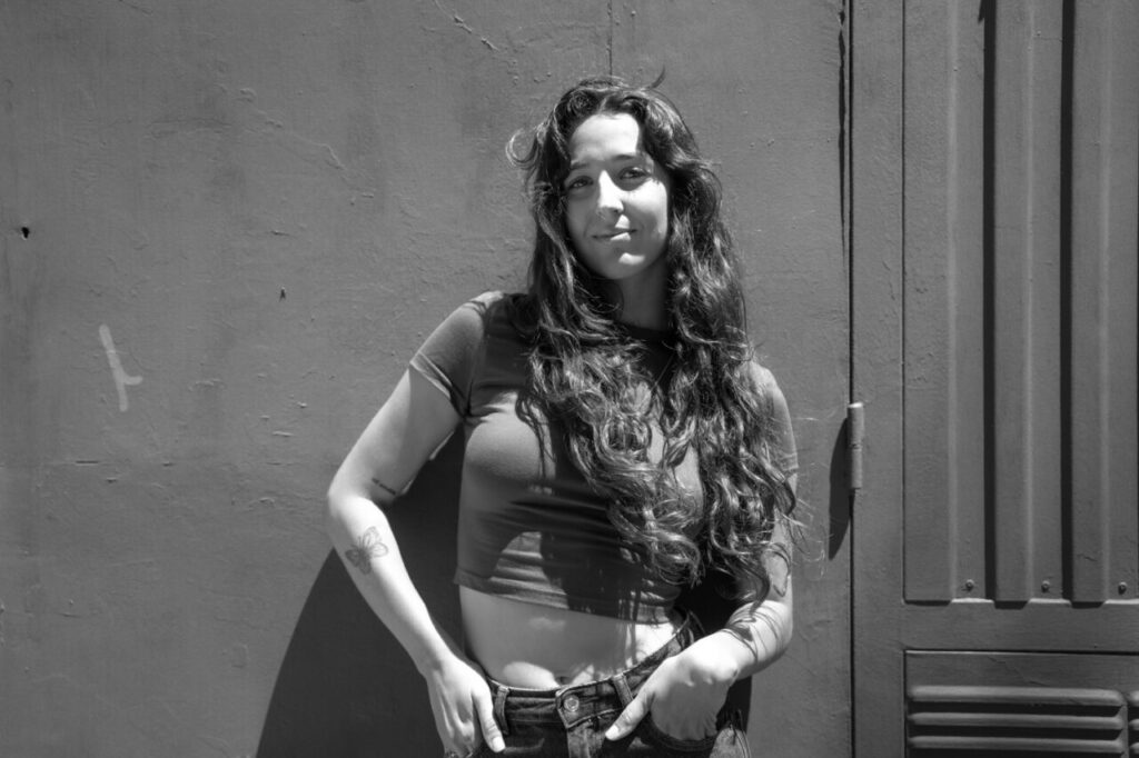 Belén Pacífico (Belucha), nominada en los MEM Awards: “El amor y el respeto por la música siguen siendo mi brújula” 2 Mujer con cabello largo y rizado posando frente a una pared