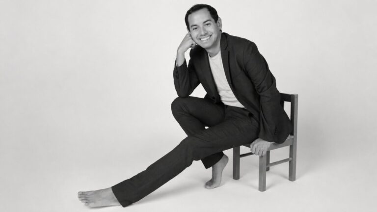 Retrato de Alex Ceball sentado en una silla con una sonrisa.