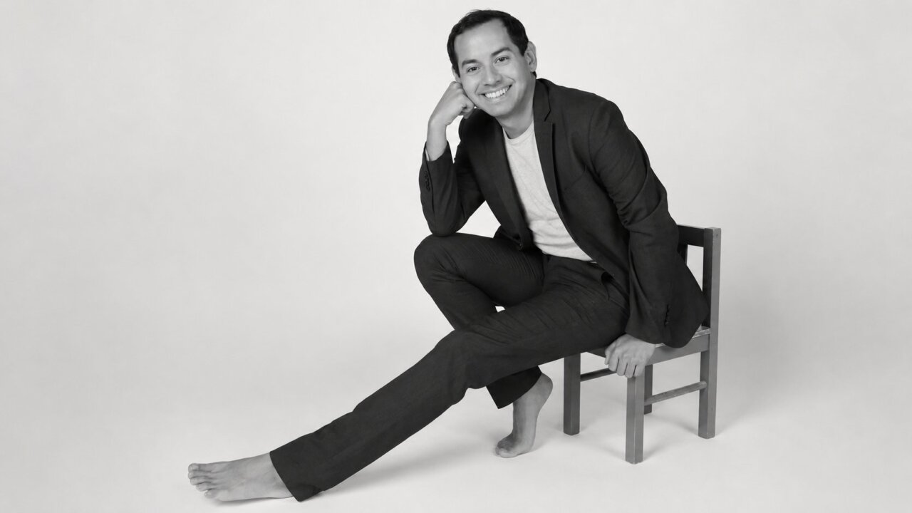 Retrato de Alex Ceball sentado en una silla con una sonrisa.