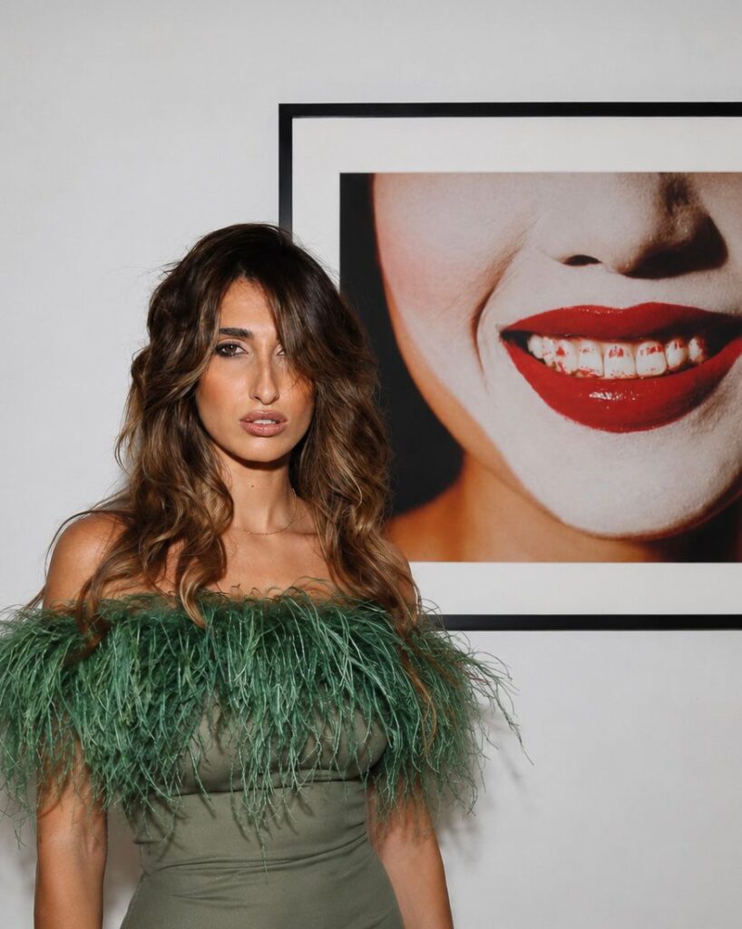 Mujer con vestido verde y plumas frente a una obra de arte