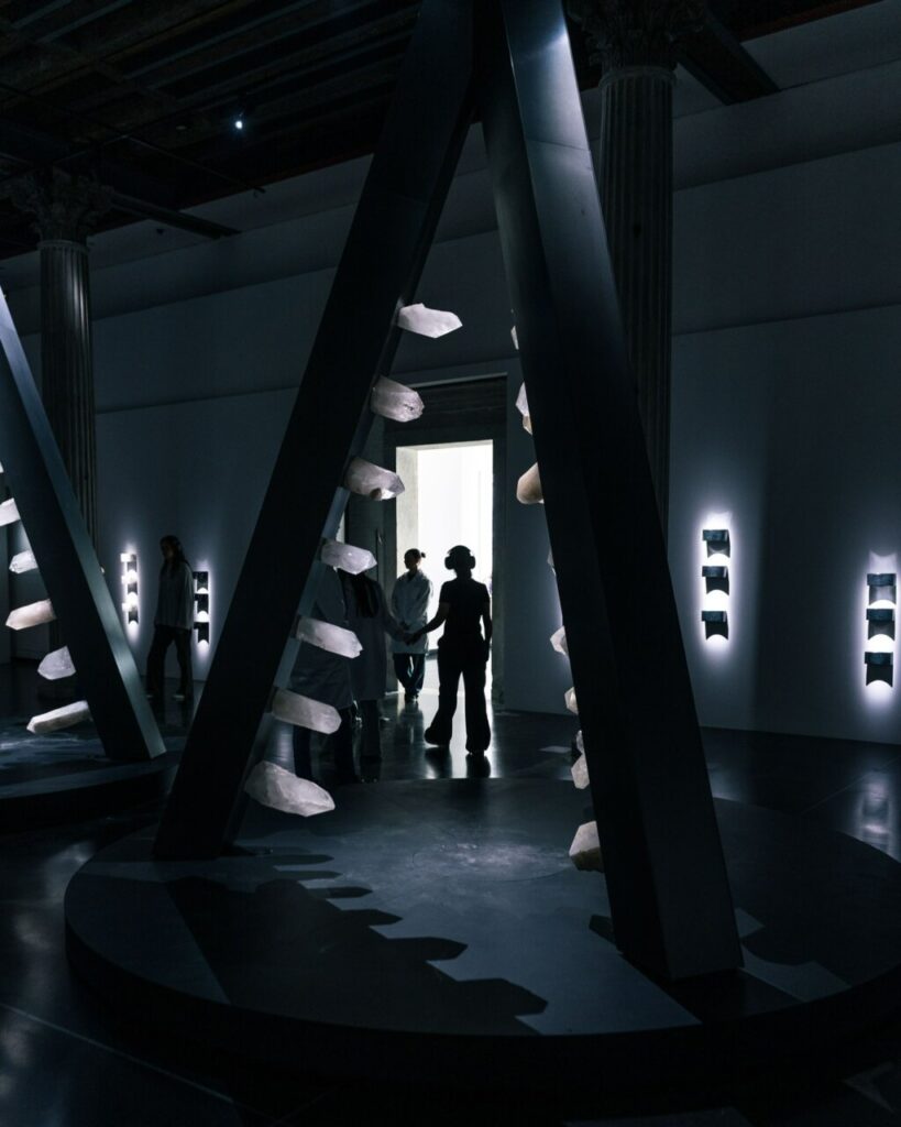 Vista de una instalación artística en la Bienal de Venecia con estructuras y visitantes.