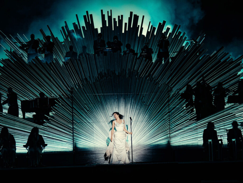 Rosalía actuando en un escenario con luces y músicos de fondo