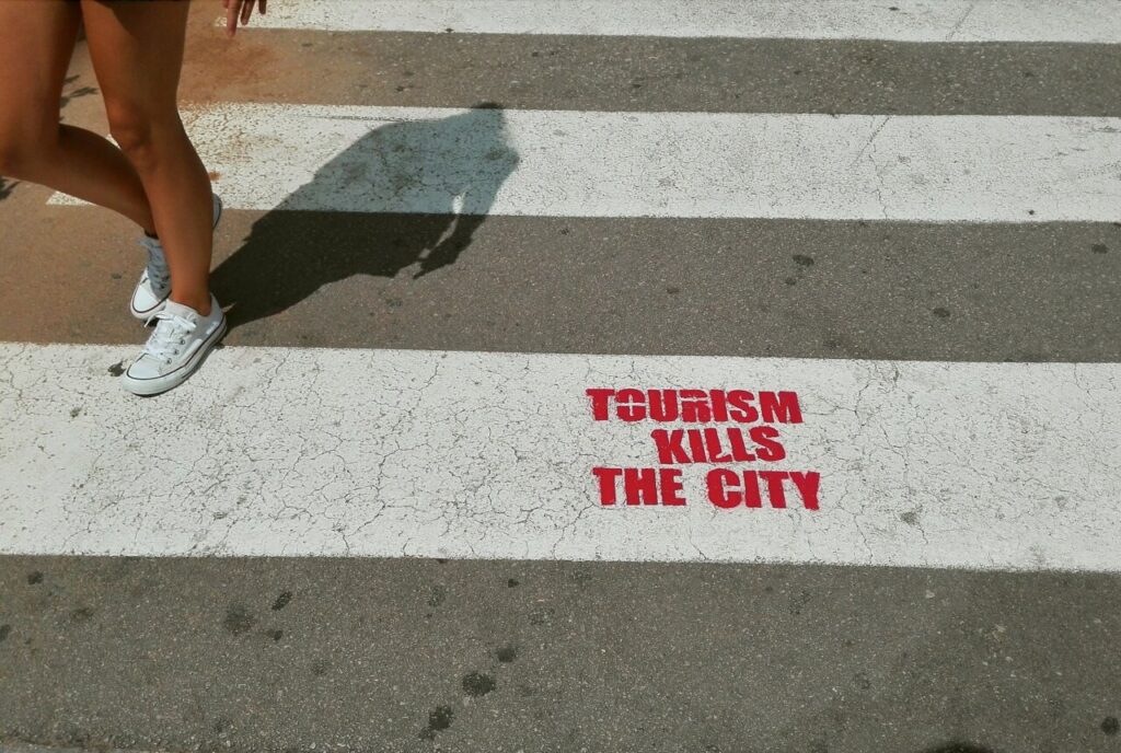 Fotografía de un paso de cebra con la frase turismo mata la ciudad.