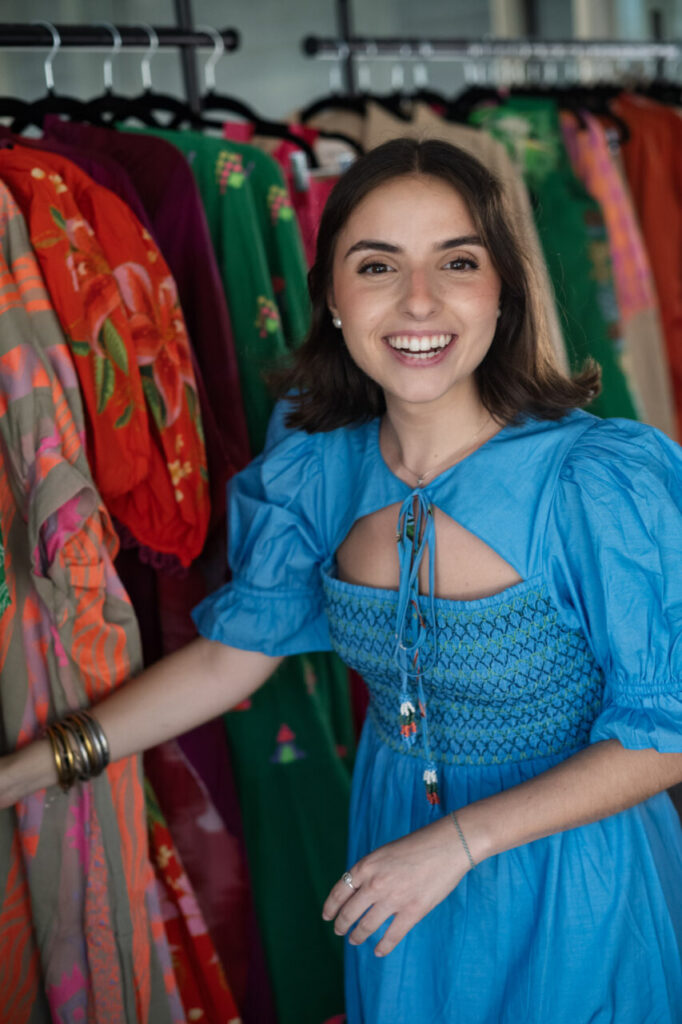 Cuando la moda se sentó frente al mar 12 Mujer sonriente con vestido azul frente a ropa colorida en una inauguración