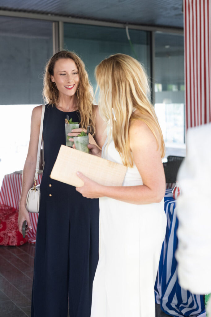 Cuando la moda se sentó frente al mar 11 Dos mujeres conversando en un evento elegante con cócteles en mano