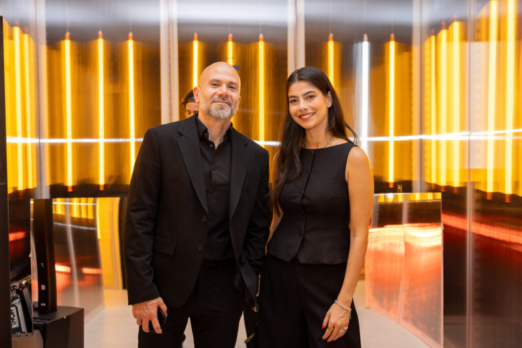 Dos personas posando en un evento de diseño con luces de fondo