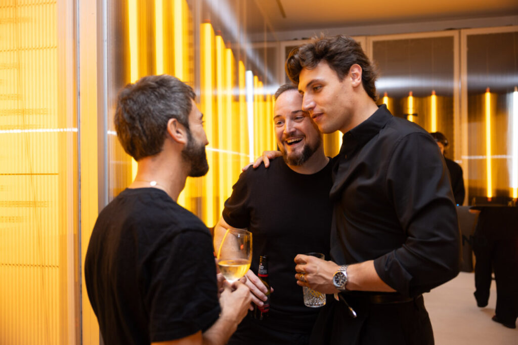 Tres hombres conversando en un evento de diseño con luces amarillas