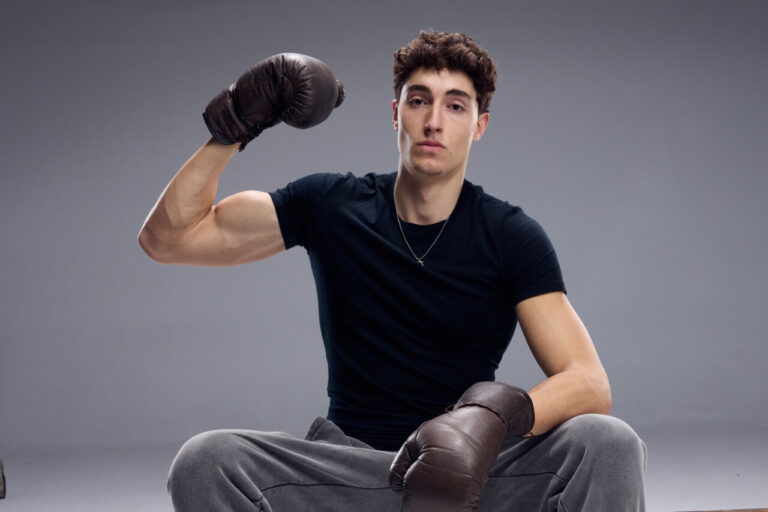 Joven boxeador sentado con guantes de boxeo en un fondo gris