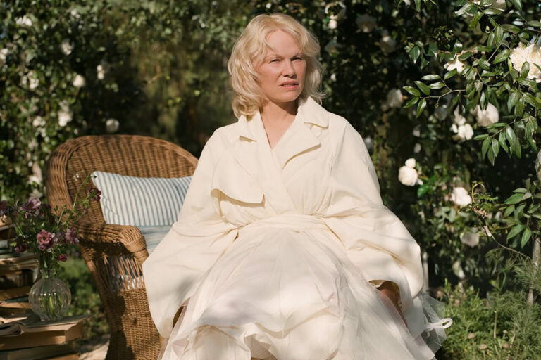 Pamela Anderson sentada en un jardín con flores y una silla de mimbre