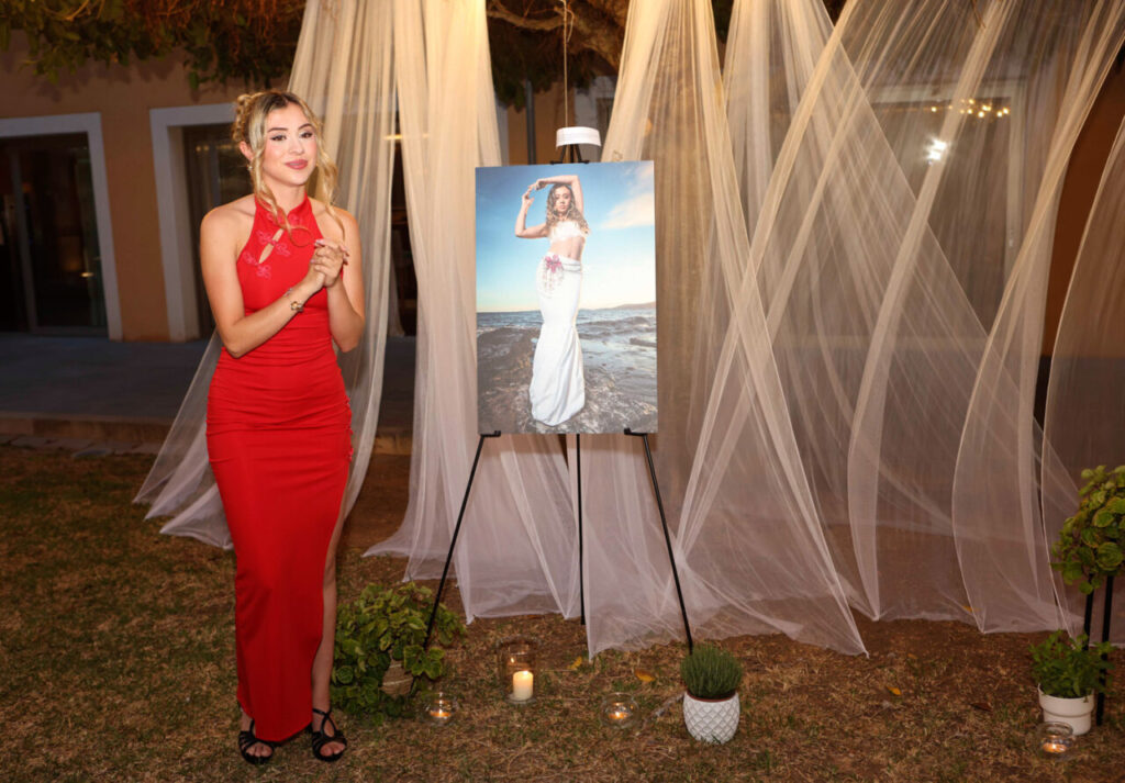 Modelo en vestido rojo junto a una fotografía en evento de graduación