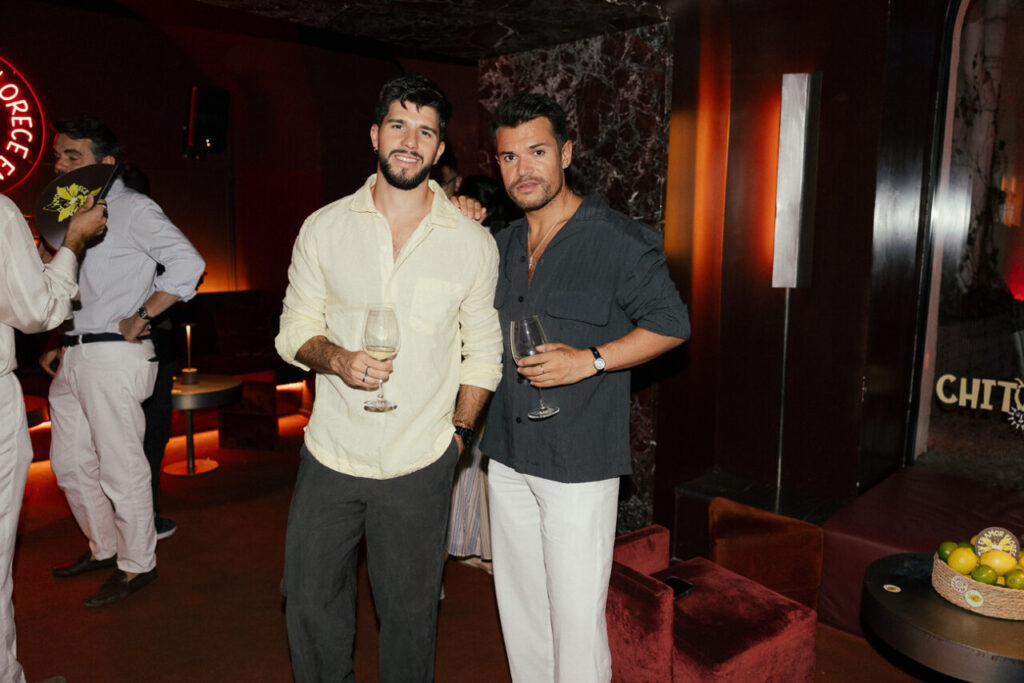 Dos hombres en una gala sosteniendo copas de vino en un ambiente elegante.
