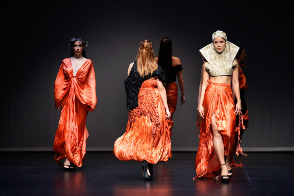 Modelos desfilando en una pasarela con vestidos naranjas brillantes