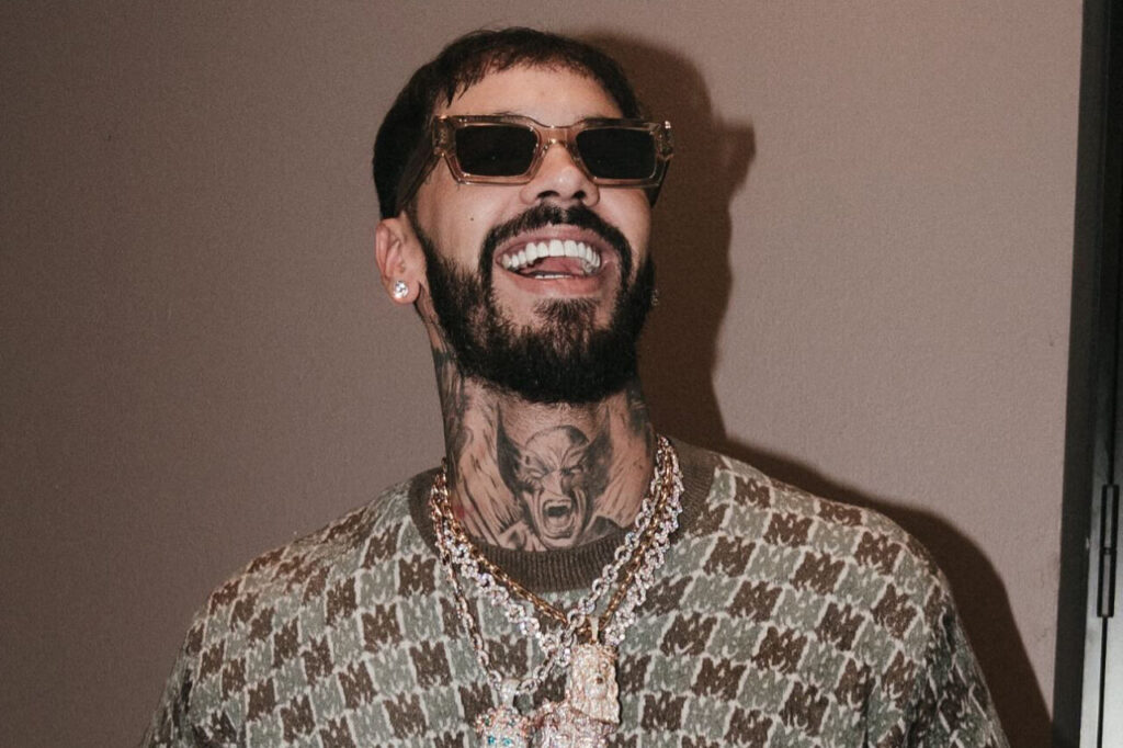 Anuel AA sonriendo con gafas de sol y joyas brillantes