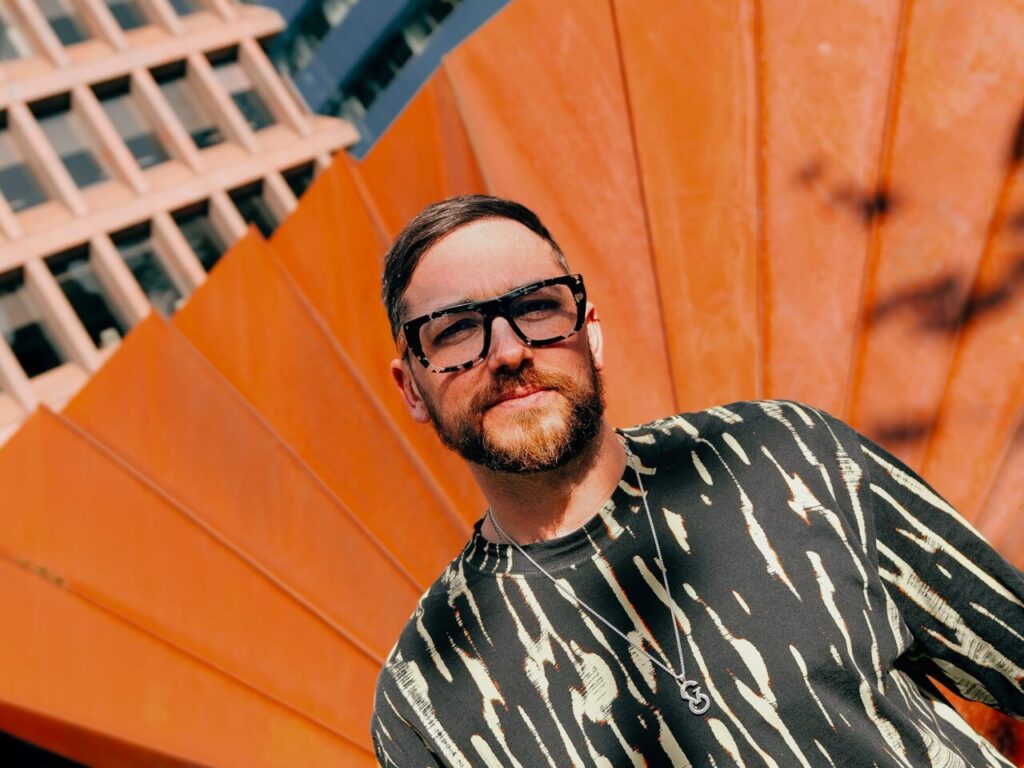 Hombre con gafas de sol frente a un fondo naranja brillante