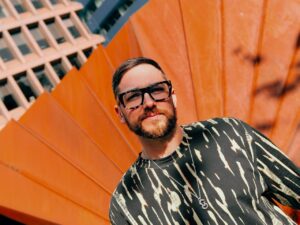 Hombre con gafas de sol frente a un fondo naranja brillante