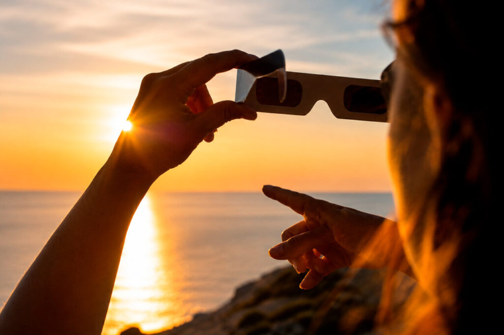 Persona sosteniendo gafas de eclipse mientras observa el sol al atardecer